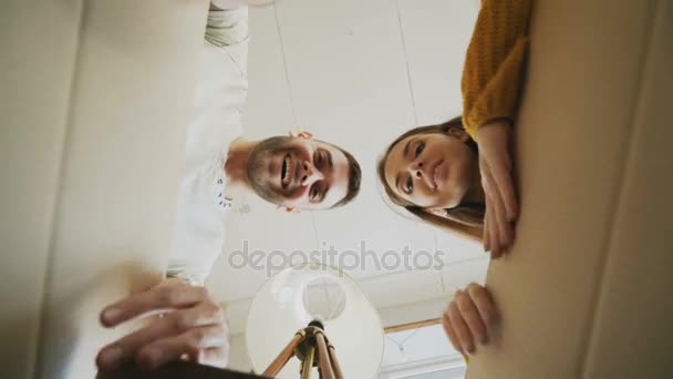 Молодая счастливая пара открывает картонную коробку и заглядывает внутрь и закрывает ее, проверяя после переезда в новый дом — стоковое видео