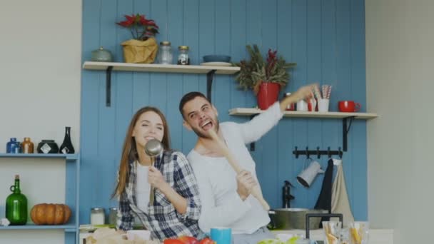 Молодые веселые пары весело танцуют и поют, готовя дома на кухне — стоковое видео