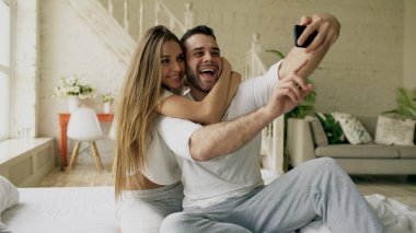 Genç güzel ve sevgi dolu çift selfie resim sabah yatakta otururken smartphone kameraya çekmek