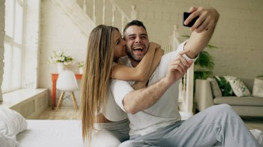Genç güzel ve sevgi dolu çift selfie resim sabah yatakta otururken smartphone kameraya çekmek