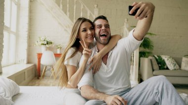 Genç güzel ve sevgi dolu çift selfie resim sabah yatakta otururken smartphone kameraya çekmek