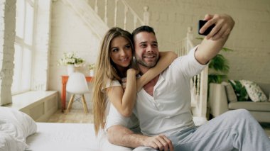 Genç güzel ve sevgi dolu çift selfie resim sabah yatakta otururken smartphone kameraya çekmek