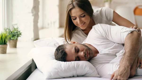 Young beautiful and loving couple wake up at the morning. Attractive woman kiss and hug his husband in bed — Stock Photo, Image