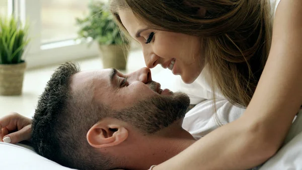 Genç gülümsemek güzel ve sevgi dolu bir çift oynamak ve sabah yatakta öp. Çekici bir adam karısını yatakta sarılma ve öpüşme