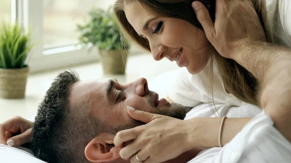 Close-up de Jovem casal bonito e amoroso jogar e beijar na cama pela manhã. Homem atraente beijando e abraçando sua esposa na cama — Fotografia de Stock