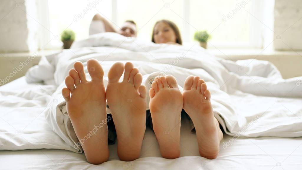 Closeup of young beautiful and loving couple play and dance their feet under blanket while wake up in bed in morning