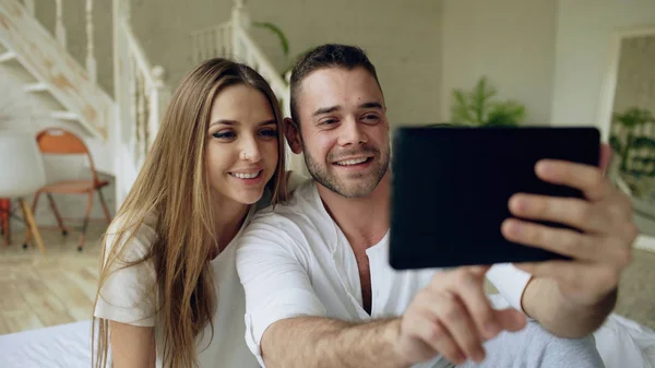 Close-up de Jovem casal bonito e amoroso ter vídeo chat segurando smartphone e conversando com amigos sentados na cama em casa — Fotografia de Stock