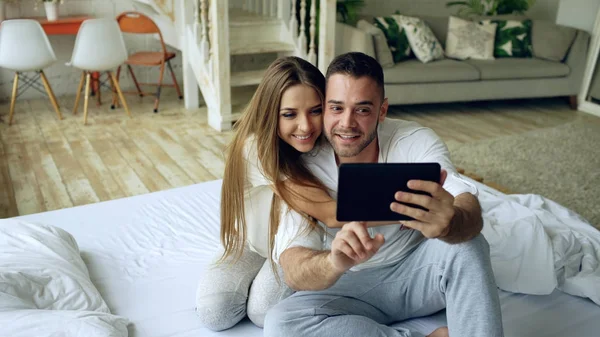 Close-up de Jovem casal bonito e amoroso ter vídeo chat segurando smartphone e conversando com amigos sentados na cama em casa — Fotografia de Stock