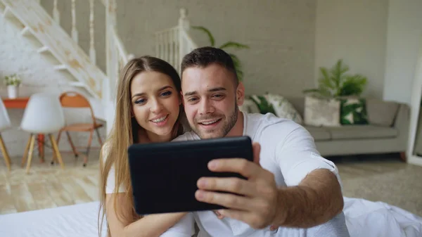 Close-up de Jovem casal bonito e amoroso ter vídeo chat segurando smartphone e conversando com amigos sentados na cama em casa — Fotografia de Stock