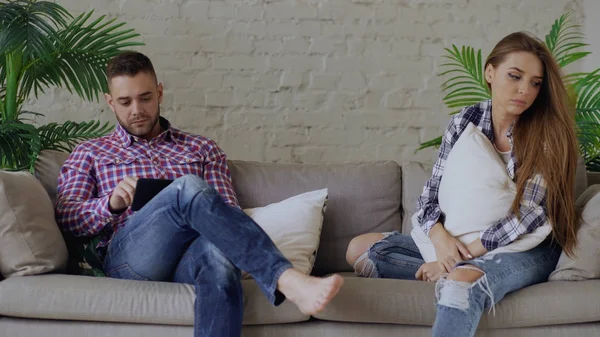 Young upset woman is stressed and unhappy while her boyfriend using tablet computer sit on couch at home — Stock Photo, Image