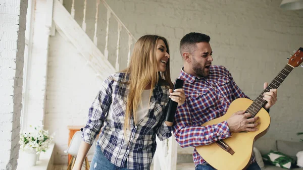 Divertida pareja feliz y amorosa bailando y tocando la guitarra. Hombre y mujer se divierten durante sus vacaciones en casa — Foto de Stock