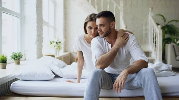 Depressiver Yong-Mann sitzt im Bett und hat Stress, während seine Freundin kommt und ihn umarmt und im Schlafzimmer zu Hause küsst — Stockfoto