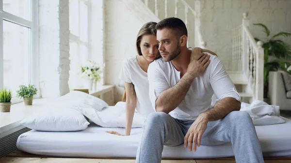 Depressed yong man sitting in bed having stressed while his girlfriend come and embrace him and kiss in bedroom at home Stock Image