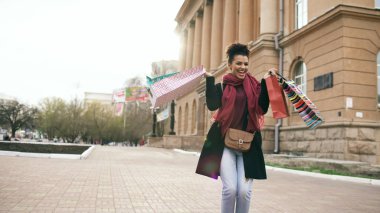 Çekici dans yarış kız karışık ve çanta ile sokakta yürürken iyi eğlenceler. Mutlu genç kadın alışveriş merkezi Satılık alışveriş sonra yürüyüş