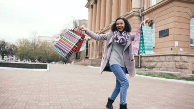 Çekici dans yarış kız karışık ve çanta ile sokakta yürürken iyi eğlenceler. Mutlu genç kadın alışveriş merkezi Satılık alışveriş sonra yürüyüş