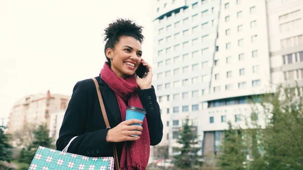 Επιχειρήσεων γυναίκα ελκυστική μικτή φυλή μιλάμε smartphone και πίνοντας τον καφέ βόλτες στην πόλη δρόμο με τσάντες αγορών — Φωτογραφία Αρχείου