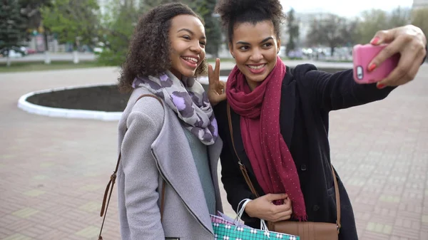 Dwa cute african american kobieta biorąc selfie z torby na zakupy i uśmiecha się. Znajomi mają zabawy po wizycie w centrum sprzedaży. — Zdjęcie stockowe