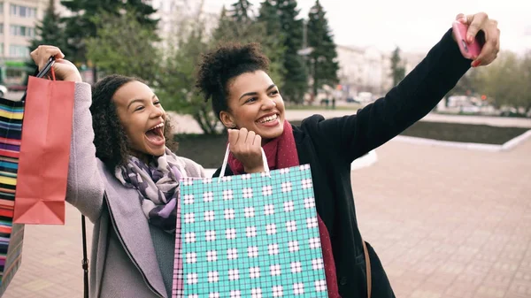 Twee schattige african american vrouw nemen selfie met boodschappentassen en glimlachen. Vrienden hebben plezier na een bezoek aan winkelcentrum verkoop. — Stockfoto