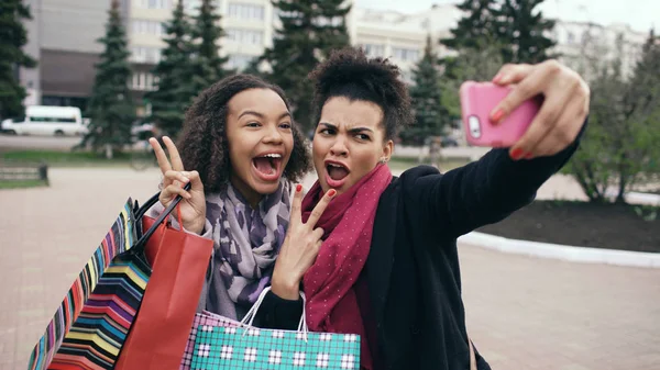 Dwa cute african american kobieta biorąc selfie z torby na zakupy i uśmiecha się. Znajomi mają zabawy po wizycie w centrum sprzedaży. — Zdjęcie stockowe