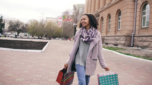 Çekici dans yarış kız karışık ve çanta ile sokakta yürürken iyi eğlenceler. Mutlu genç kadın alışveriş merkezi Satılık alışveriş sonra yürüyüş