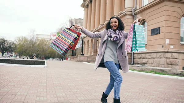Çekici dans yarış kız karışık ve çanta ile sokakta yürürken iyi eğlenceler. Mutlu genç kadın alışveriş merkezi Satılık alışveriş sonra yürüyüş