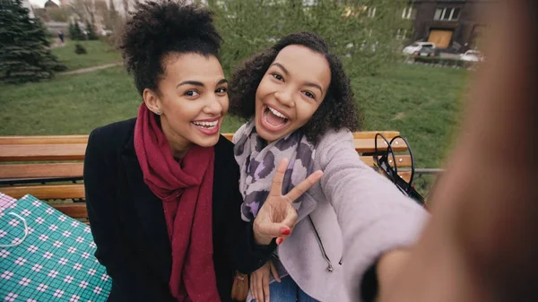 Två söta afroamerikanska kvinnan tar selfie på smartphone med kassar och leende. Flickvänner som sitter på gatan bänk ha kul efter att ha besökt mall försäljning — Stockfoto