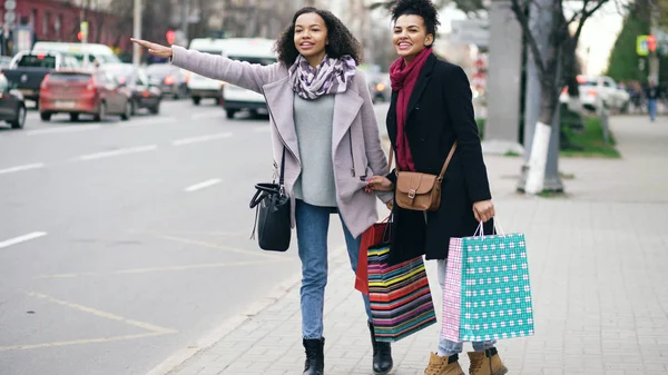两个非洲裔美国美女与购物袋呼吁的士驾驶室时从商场销售回来 — 图库照片