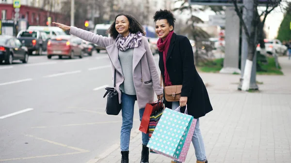 Zwei attraktive afrikanisch-amerikanische Frauen mit Einkaufstaschen, die auf dem Rückweg von einem Einkaufszentrum nach einem Taxi rufen — Stockfoto