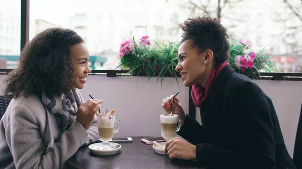 İki çekici konuşan ve içme kahve sokak Cafe yarış bayanlar karışık. Arkadaşlar alışveriş merkezi satış ziyaret ettikten sonra iyi eğlenceler — Stok fotoğraf