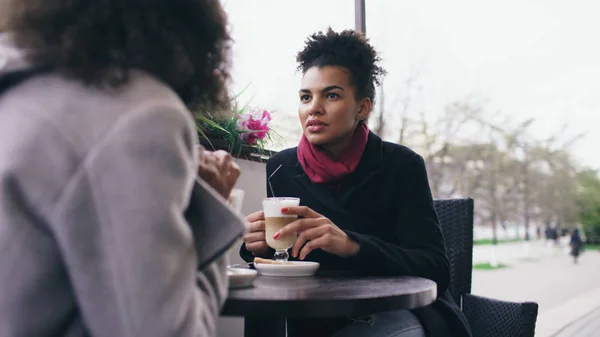 Dos atractivas mujeres de raza mixta hablando y tomando café en la cafetería de la calle. Amigos se divierten después de visitar la venta del centro comercial —  Fotos de Stock