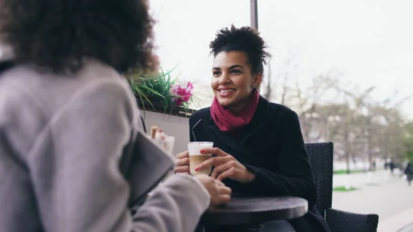 Dos atractivas mujeres de raza mixta hablando y tomando café en la cafetería de la calle. Amigos se divierten después de visitar la venta del centro comercial —  Fotos de Stock