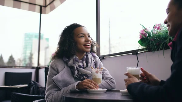 Dos atractivas mujeres de raza mixta hablando y tomando café en la cafetería de la calle. Amigos se divierten después de visitar la venta del centro comercial —  Fotos de Stock