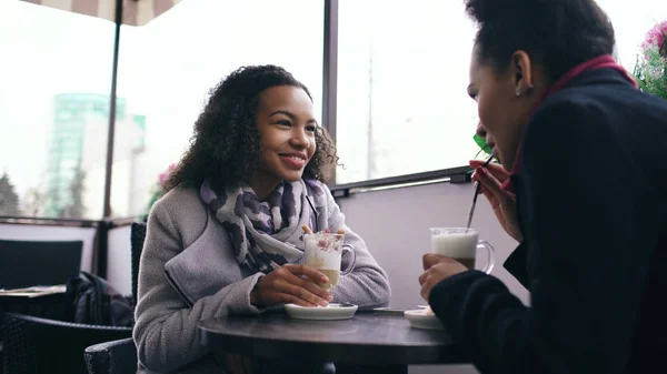 Dos atractivas mujeres de raza mixta hablando y tomando café en la cafetería de la calle. Amigos se divierten después de visitar la venta del centro comercial — Foto de Stock