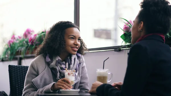 Dos atractivas mujeres de raza mixta hablando y tomando café en la cafetería de la calle. Amigos se divierten después de visitar la venta del centro comercial — Foto de Stock