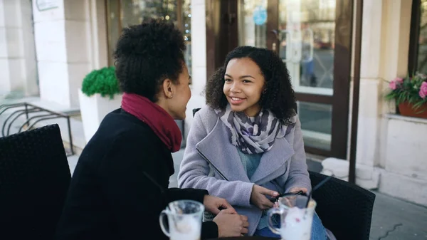 Dos atractivas mujeres de raza mixta hablando y tomando café en la cafetería de la calle. Amigos se divierten después de visitar la venta del centro comercial — Foto de Stock