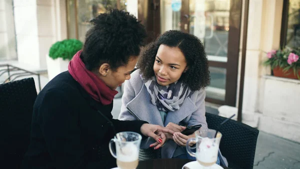 Dva atraktivní Smíšené rasy kamarádky sdílení pomocí smartphone v pouliční kavárně venku — Stock fotografie