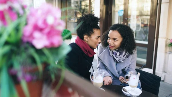 Dos atractivas amigas de raza mixta compartiendo juntos el uso de smartphone en la cafetería al aire libre —  Fotos de Stock