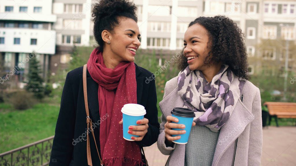 Two beautiful mixed race woman friends drink coffee and talks after shopping and walking city street