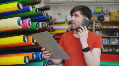 Konuşmak smartphone ve stok kontrol ambar genç işçi. Adam reklam malzemeleri satış bölümünde İnşaat