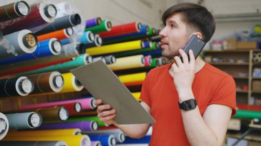 Konuşmak smartphone ve stok kontrol ambar genç işçi. Adam reklam malzemeleri satış bölümünde İnşaat