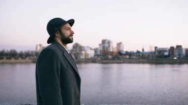 Şapkanı ve Paltonu cityscape izliyor ve Riverside'da dururken hayal turist adam genç sakallı