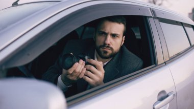 Arabanın içinde oturan ve dslr fotoğraf makinesi ile çekim genç özel dedektif adam