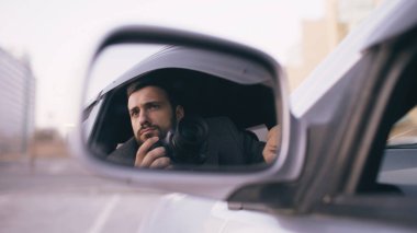 Genç özel dedektif adam arabanın içinde oturan ve dslr fotoğraf makinesi ile fotoğrafını yan aynada yansıması