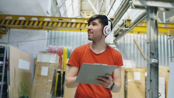 Fröhlicher junger Arbeiter in einem Industrielager, der während der Arbeit Musik hört. Mann mit Kopfhörer hat Spaß am Arbeitsplatz. — Stockfoto