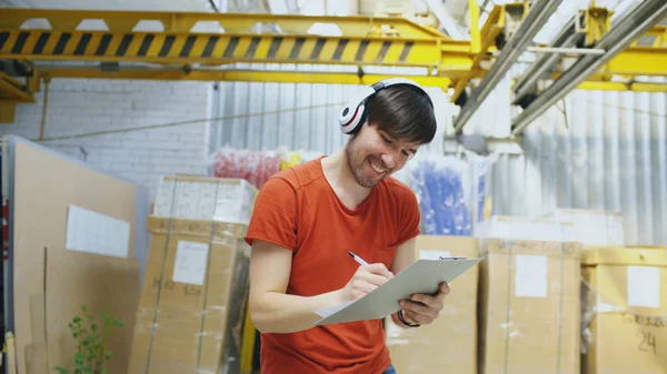Fröhlicher junger Arbeiter in einem Industrielager, der während der Arbeit Musik hört und tanzt. Mann mit Kopfhörer hat Spaß am Arbeitsplatz. — Stockfoto