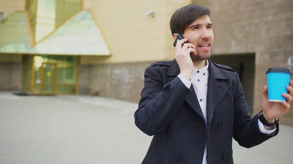 Dolly shot de jeune homme d'affaires souriant parlant sur smartphone et se sent heureux de faire affaire promenades près des immeubles de bureaux — Photo