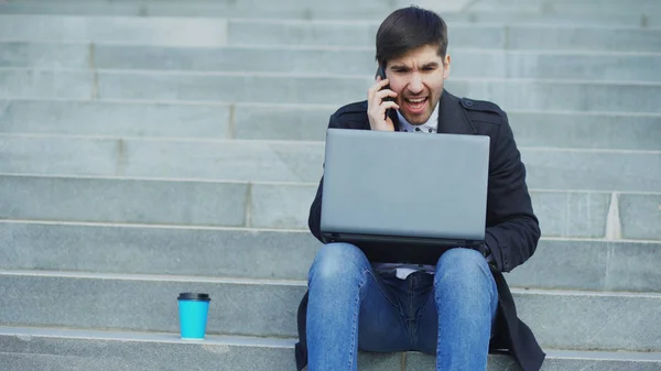 Young business man with laptop computer having stress after phone call and sitting on stairs in street. Businessman having deal problems at work concept — Stock Photo, Image