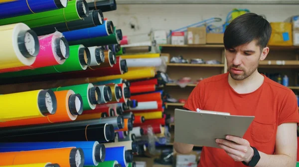 Jeune travailleur dans un entrepôt avec presse-papiers vérifier l'inventaire. Homme travaille dans le département des ventes de matériel publicitaire — Photo