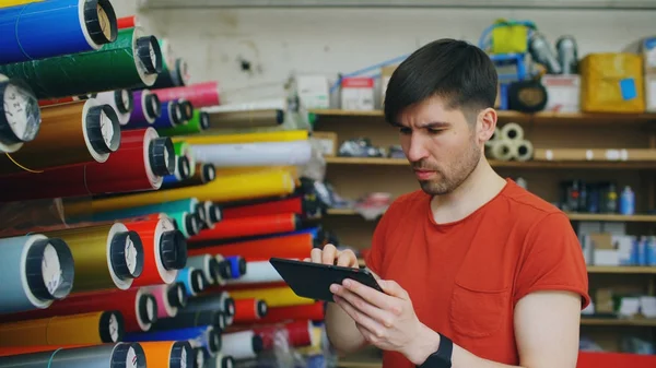 Trabajador joven en el almacén con el inventario de comprobación de tableta. El hombre trabaja en el departamento de ventas de materiales publicitarios — Foto de Stock