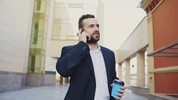 Obchodní muž mluví na mobil uzavírat dohody a chůze nedaleko moderní kancelářské budovy — Stock fotografie